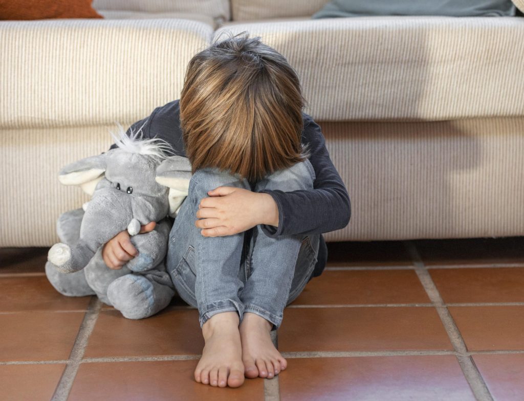 bambino triste da solo con un pupazzo in mano e la testa piegata